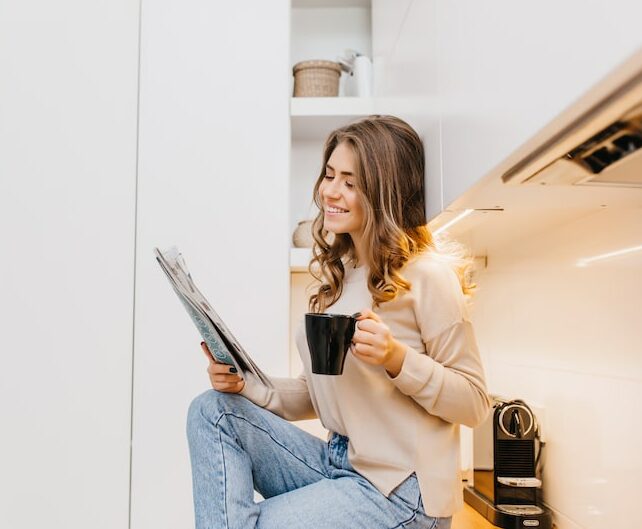 joyful-dark-haired-lady-spending-morning-at-home-reading-newspaper-with-smile-indoor-photo-of-carefree-girl-in-jeans-enjoying-tea-in-kitchen